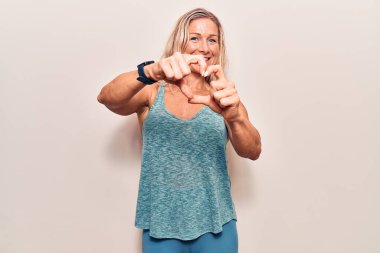 Orta yaşlı, beyaz kadın spor giysisi giymiş, aşıkken gülümseyen, elleriyle kalp sembolü yapan. romantik kavram. 