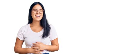 Genç, güzel Asyalı bir kız, günlük kıyafetler ve gözlük takıyor, gülümsüyor ve kahkahalar atıyor.. 