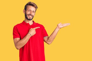 Sarışın, sakallı, sıradan giyinen yakışıklı adam kameraya hayret ediyor ve gülümsüyor.. 