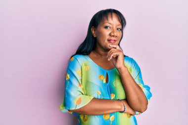 Orta yaşlı Afro-Amerikalı kadın, günlük kıyafetler giyip kameraya kollarını kavuşturup, çenesini kapatarak gülümsüyor. Olumlu düşünmek. 