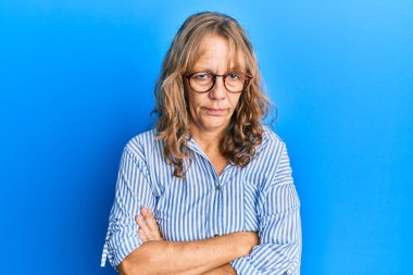 Sıradan kıyafetler giyen, gözlüklü, kuşkucu ve gergin orta yaşlı sarışın bir kadın. Yüzünde çapraz kollu tasvip etmeyen bir ifade var. negatif kişi. 