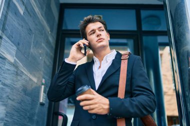 Kafkasyalı genç iş adamı ciddi bir ifadeyle akıllı telefondan konuşuyor ve şehirde kahve içiyor..