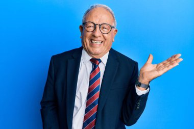 Beyaz üst düzey bir adam iş elbisesi ve kravat takıyor. Gülümsüyor, eli avucunda kameraya bakıyor.. 