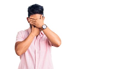 Yakışıklı Latin Amerikalı genç adam gündelik yazlık tişört giyiyor gözlerini ve ağzını ellerinle kapatıyor, şaşırmış ve şok olmuş. duygu gizleme 