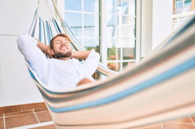 Yakışıklı beyaz adam mutlu bir şekilde gülerek terasta dinleniyor.