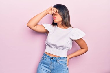 Genç, güzel, esmer, günlük kıyafetler giyen bir kadın izole edilmiş pembe arka planda dikiliyor.