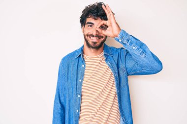 Kıvırcık saçlı ve ayı gibi sıradan bir kot ceket giyen yakışıklı genç adam. El hareketleriyle gülümsüyor, gözleriyle mutlu yüzüyle parmaklarının arasından bakıyor.. 