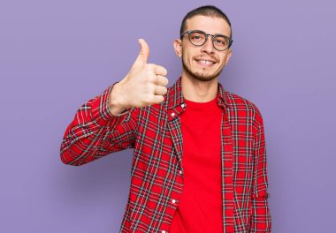 İspanyol genç adam gündelik giysiler giyip mutlu mesut el hareketi yapıyor. Kameraya bakıp başarıyı gösteren ifade. 