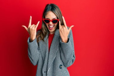 Young brunette woman wearing fashion and modern look shouting with crazy expression doing rock symbol with hands up. music star. heavy concept. 