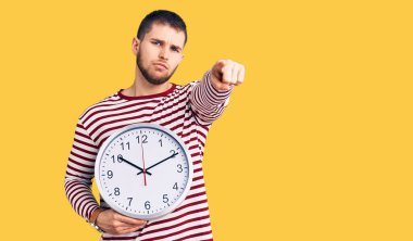 Elinde koca bir saat tutan yakışıklı bir adam kamerayı işaret ediyor ve sen kendine güvenen ciddi bir hareket yapıyorsun. 