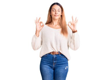 Güzel, genç bir kadın günlük kıyafetler giyiyor rahatlıyor ve gözleri kapalı gülümsüyor parmaklarıyla meditasyon hareketi yapıyor. yoga konsepti. 