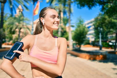 Genç sarışın sporcu. Parkta egzersiz yaparken kulaklık takıyor..