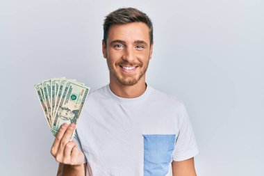 Yakışıklı beyaz adam elinde 20 dolarlık banknot tutuyor. Pozitif ve mutlu görünüyor. Kendine güvenen bir gülümsemeyle dişlerini gösteriyor. 