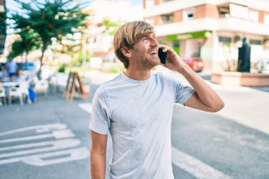 Yakışıklı beyaz adam dışarıda mutlu bir şekilde gülümsüyor telefonda konuşuyor.