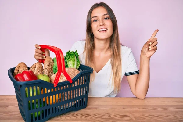 Beautiful Caucasian Woman Holding Supermarket Shopping Basket Smiling Happy Pointing — Stock Photo, Image