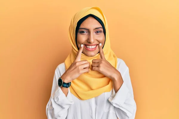 若いですブルネットArab女性身に着けています伝統的なイスラムヒジャーブスカーフ笑顔でオープン口 指を指すと明るい笑顔を強制 — ストック写真