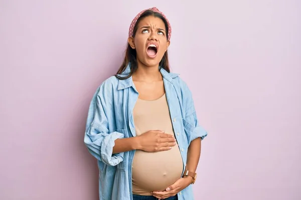 赤ん坊を期待している美しいヒスパニック系の女性 妊娠中の腹に触れる怒っていると怒っている叫び不満と激怒 怒りを見上げと叫んで — ストック写真