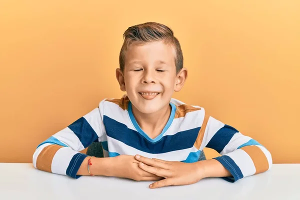 面白い表情で幸せ舌を突き出してテーブルの上に座ってカジュアルな服を着て愛らしい白人の子供 感情の概念 — ストック写真