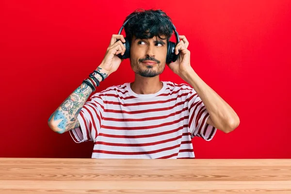 Junger Hispanischer Mann Mit Kopfhörern Sitzt Auf Dem Tisch Lächelt — Stockfoto