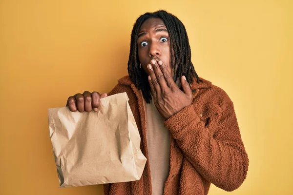 Африканский Американец Косичками Держащий Бумажный Пакет Закрывающий Рот Рукой Шокирован — стоковое фото