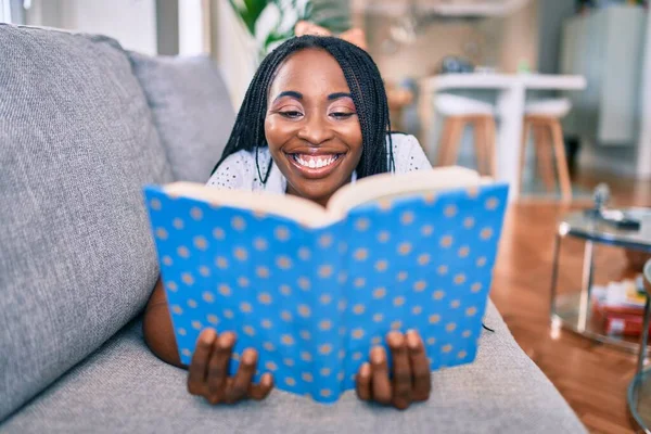 Joven Mujer Afroamericana Sonriendo Feliz Tendida Libro Lectura Del Sofá — Foto de Stock