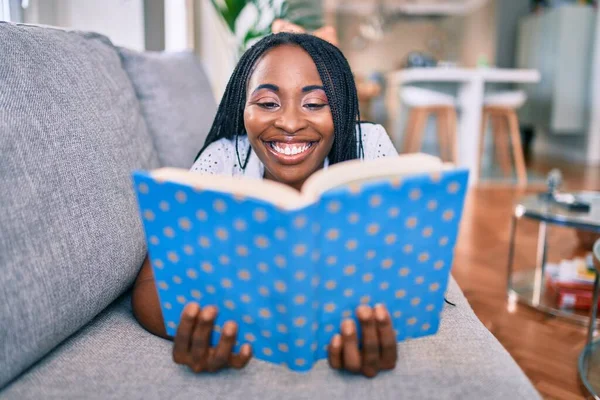 Jovem Afro Americana Sorrindo Feliz Deitado Sofá Leitura Livro Casa — Fotografia de Stock