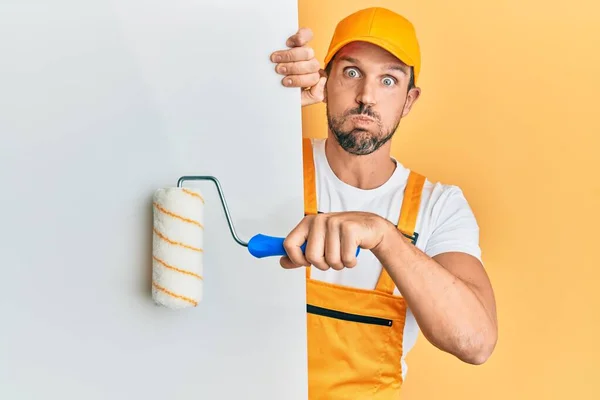 Young Handsome Man Holding Roller Painter White Banner Puffing Cheeks — Stock Photo, Image