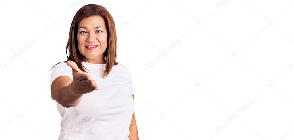 Middle age latin woman wearing casual white tshirt smiling friendly offering handshake as greeting and welcoming. successful business. 