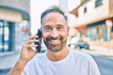 Orta yaşlı yakışıklı adam şehirde akıllı telefon kullanarak mutlu gülümsüyor..