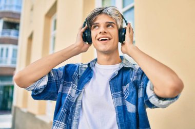 Genç İspanyol adam şehirde akıllı telefon ve kulaklık kullanarak mutlu gülümsüyor..