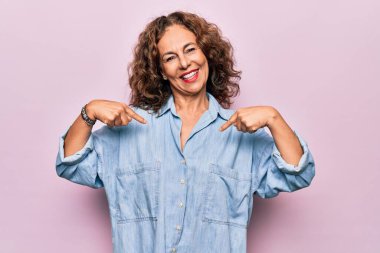 Orta yaşlı, güzel bir kadın pembe arka plan üzerinde dikilmiş, kendine güvenen, yüzünde bir gülümsemeyle, gururlu ve mutlu bir şekilde kendini gösteren..