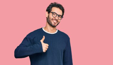 Gündelik giysiler ve gözlük takan İspanyol genç adam elleriyle mutlu bir jest yapıyor. Kameraya bakıp başarıyı gösteren ifade. 