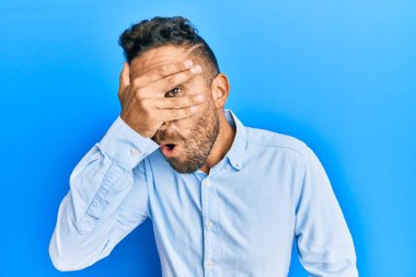 Sakallı yakışıklı bir adam, günlük giysiler giymiş. Şoka girmiş, yüzünü ve gözlerini kapamış, utanmış bir ifadeyle parmaklarının arasından bakıyor.. 