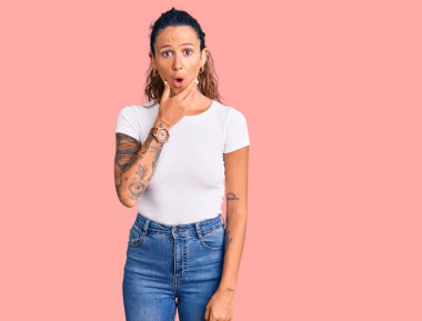 Gündelik beyaz tişörtlü İspanyol bir kadın. İnançsızlıktan, şaşkınlıktan ve elleri çenesinde büyülenmiş bir ifade takınıyor. 