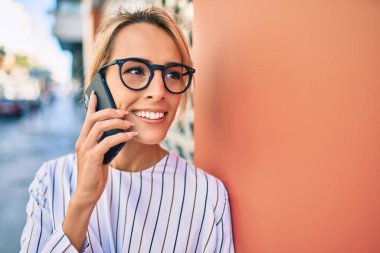 Genç sarışın iş kadını şehirde akıllı telefon kullanarak mutlu bir şekilde gülümsüyor..