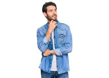 Elleri çenesinde gündelik giysiler içinde soru soran genç İspanyol bir adam, düşünceli bir ifade. Gülümseyen ve düşünceli bir yüz. şüphe kavramı. 