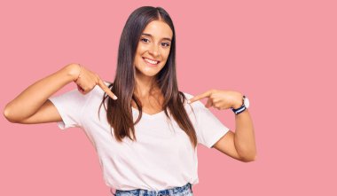 Genç İspanyol kadın, günlük beyaz tişört giyiyor. Kendine güvenen, yüzünde gülümseme olan, kendini gururlu ve mutlu bir şekilde gösteren.. 