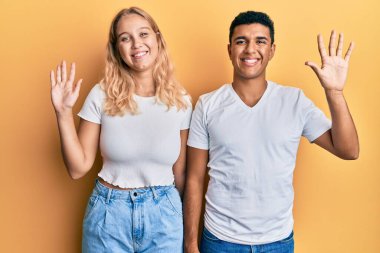 Irklar arası genç çift, günlük beyaz tişörtler giyerek on numarayı gösterip işaret ederken kendinden emin ve mutlu bir şekilde gülümsüyor.. 