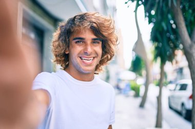 Genç, yakışıklı İspanyol gülümseyen adam şehrin caddesinde fotoğraf çekerken mutlu oluyor.