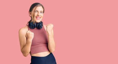 Güzel beyaz kadın spor kıyafetleri giyiyor ve kulaklık takıyor. Şaşırmış ve şaşırmış bir şekilde kolları açık ve gözleri kapalı bir şekilde başarıyı kutluyor. Kazanan konsept. 