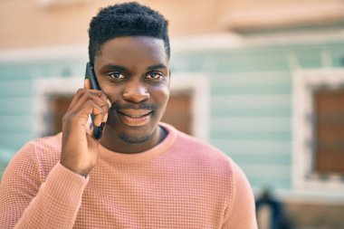Genç Afrikalı Amerikalı gülümseyen mutlu bir adam şehirdeki akıllı telefondan konuşuyor..