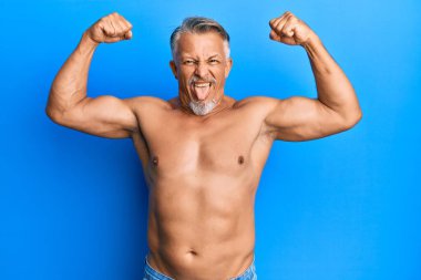 Orta yaşlı, gri saçlı, üstsüz, jest yapan, komik bir ifadeyle dilini dışarı çıkaran bir adam.. 