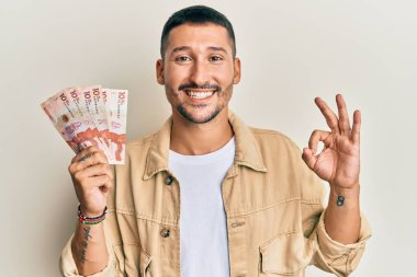 Elinde 10 Kolombiya pezosu olan yakışıklı adam parmaklarıyla imza atıyor, gülümsüyor ve mükemmel bir sembol oluşturuyor. 