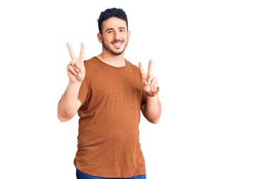 Gündelik kıyafetler giyen genç İspanyol adam kameraya bakıp zafer işareti yaparken parmaklarını gösteriyor. İki numara.. 