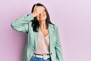 Orta yaşlı esmer kadın, sıradan kıyafetler giyiyor, gülümsüyor ve elleri yüzünde şaşkınlıktan gözleri kapatıyordu. kör kavram. 