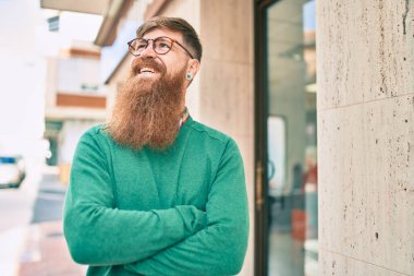 Kollarını kavuşturmuş genç İrlandalı adam gülümseyerek şehirde mutlu mesut yürüyor..