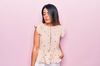 Genç, güzel, esmer, günlük kıyafetler giyen bir kadın izole edilmiş pembe arka planda dikiliyor.