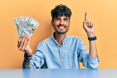 Masada dolarları tutan genç İspanyol bir adam bir fikir ya da soruyla gülümsüyor ve mutlu bir yüzle işaret ediyor. 