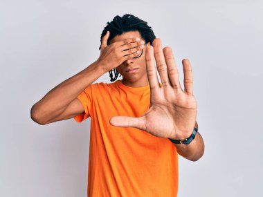 Genç Afro-Amerikalı bir adam günlük kıyafetler ve gözlük takıyor. Gözlerini ellerle kapatıyor ve üzgün ve korku dolu ifadelerle jestleri durduruyor. utangaç ve olumsuz kavram. 