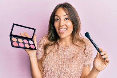 Genç esmer kadın elinde makyaj fırçası ve allık tutan komik bir ifadeyle mutlu bir dille.. 